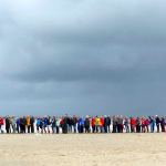 Een groep mensen op het strand, netjes in een rijtje